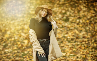 Image-shot of a young attractive woman wearing a coat and felt hat on blurry background of fallen leaves in the autumn park