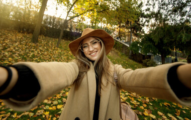 Selfie portrait of a funny young woman on the background of fallen leaves in the park. Autumn time