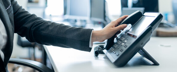 Close-up of a female employee's hand on a landline phone. Woman picks up a push-button telephone at the workplace in the office