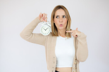 Portrait of positive pretty young woman in casual sweater pointing at wall clock over white background