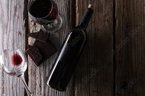 Top view of elegant bottle and wineglasses with red wine and dark chocolate on rustic wooden background. Wine and dessert. Template concept for your design and advertising company promotion.