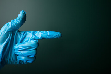 Pointing hand in blue medical glove on dark background