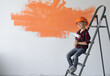 © Andrii Lysenko - boy dressed in protective orange sits on a construction ladder.