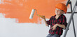 © Andrii Lysenko - a boy dressed in protective orange sits on a construction ladder points with a roller to an empty space for text.