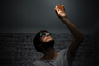 © Lalandrew - Dark portrait of young guy, looking up and touching the light. Wearing sunglasses. Using wireless earphones.