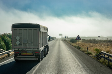 Wall Mural - Tipper truck driving down the straight of a highway with a bank of fog in the background.