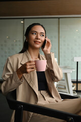 Shot of business young woman talking on mobile phone while holding coffee cup in the office.