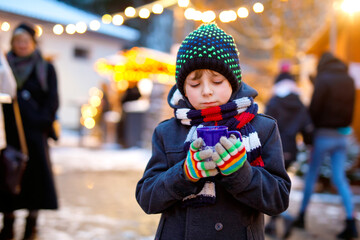 Wall Mural - Little cute kid boy drinking hot children punch or chocolate on German Christmas market. Happy child on traditional family market in Germany, Laughing boy in colorful winter clothes