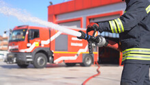 A Fireman Keeps Fire Hose And Extinguishes Fire For Training. Fire Station Background.