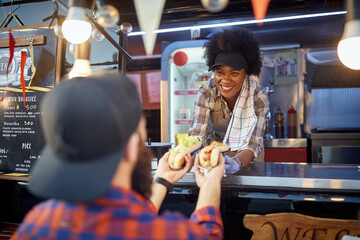 young afro-american employee giving with smile sandwiches through a fast food window to a satisfied 