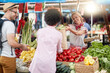 © luckybusiness - Seller woman offers fresh and organic vegetables at the green market or farmers market stall.  Young buyers choose and buy products for healthy food in grocery. All for diet healthy eating, lifestyle.