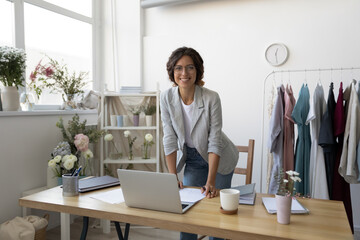 Portrait of smiling young Caucasian successful female fashion designer pose at modern cozy home office desk. Happy confident millennial businesswoman stylist or tailor work at creative workplace.