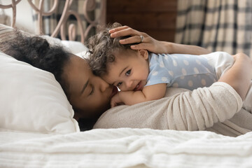 Wall Mural - loving young biracial mom lying in cozy bed hug cuddle cute little baby toddler. caring happy africa