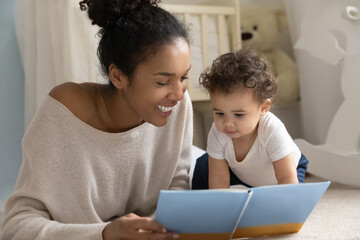 Wall Mural - happy young biracial mom and little ethnic toddler child sit on floor in children room at home readi