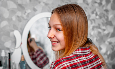 portrait of young teenager girl with long hair combing her hair in front of her mirror.