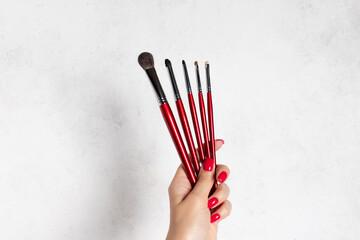 woman's hand with red nail design holding makeup brush set. Makeup Accessories. white background with copy space.