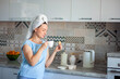 © borisenkoket - Happy woman with a towel on her head sutra drinks coffee with cookies for breakfast in his own kitchen at home
