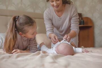 Mother holding infant baby, take care of her 3 months old child at home bedroom . Happy mom carying of her newborn son . Mother and elder sister kissing the boy