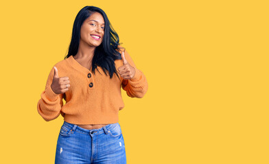 Hispanic woman with long hair wearing casual winter sweater success sign doing positive gesture with hand, thumbs up smiling and happy. cheerful expression and winner gesture.