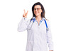 © Krakenimages.com - Young beautiful woman wearing doctor stethoscope and glasses showing and pointing up with fingers number two while smiling confident and happy.
