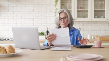 Wall Mural - Senior older woman holding bill using calculator and laptop paying online managing finances, calculating fees rates, planning banking loan retirement pension payment sitting at home kitchen table.