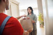 © insta_photos - Indian woman customer taking delivery paper eco bag with grocery takeout food meal from man courier holding paper package delivering supermarket or restaurant takeaway order standing at door at home.