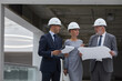 © Seventyfour - Waist up portrait of three successful business people wearing hardhats and holding plans while inspecting construction site indoors, copy space