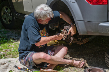 Drive way mechanic male works on his brakes in his own driveway to save money 