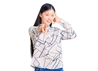 Sticker - Young beautiful chinese woman wearing casual shirt smiling doing talking on the telephone gesture and pointing to you. call me.