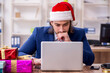 © Elnur - Young male employee working in the office at Christmas Eve