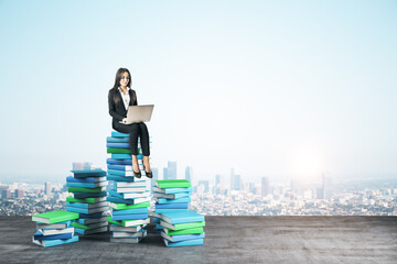 Wall Mural - Young businesswoman with laptop computer sitting on books