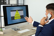 © New Africa - Office worker in front of computer with warning about virus attack on screen