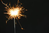 Fototapeta Sypialnia - Bright burning sparkler on black background, closeup. Space for text
