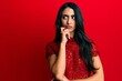 © Krakenimages.com - Beautiful hispanic woman wearing elegant clothes over red background serious face thinking about question with hand on chin, thoughtful about confusing idea