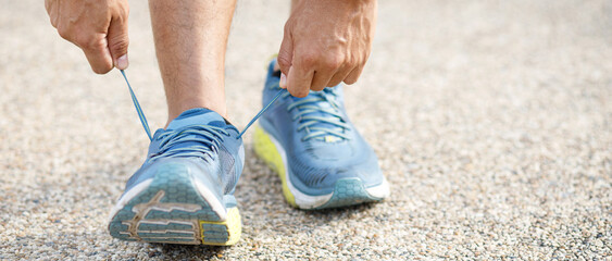 Wall Mural - Running shoes. close up male athlete tying laces for jogging on road. Runner ties getting ready for training. Sport lifestyle. copy space banner.