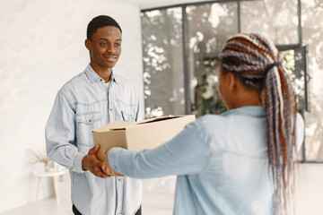 Wall Mural - Young couple moving in to new home together. African american couple with cardboard boxes.