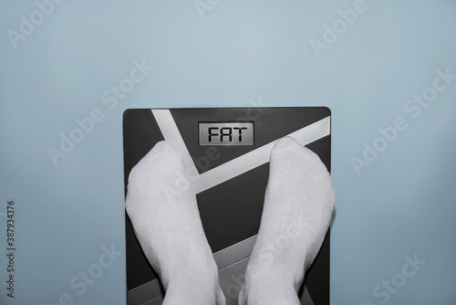 Person on electronic scales, display shows Fat. Overweight, obesity, lazy lifestyle, diet concept. Top view, pov