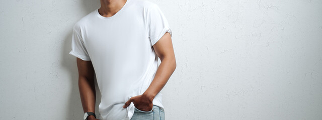 Wall Mural - Smiling asian man in white blank t-shirt, grunge wall, studio portrait. Wide screen, panoramic