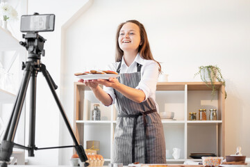 Sticker - Christmas bakery food. Online greeting. Homemade cookies. Virtual communication. Happy woman showing festive gingerbread pastries on smartphone tripod light home kitchen interior.