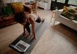 © StratfordProductions - High angle view of woman watching video on laptop while exercising on yoga mat at home