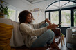 © StratfordProductions - Smiling young woman relaxing on couch at home holding tv remote control