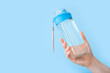 Drinking water bottle for sports in female hand on blue backgraund with copy space. Reusable bottle. Healthy lifestyle and fitness concept
