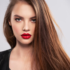 Wall Mural - Portrait of beautiful young woman with bright makeup. Beautiful brunette with bright red lipstick on her lips. Pretty girl with long brown hair. Brunette dressed in a black leather jacket. Sexy girl
