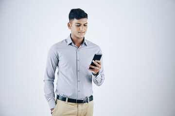 Positive handsome young Indian businessman reading text messages on smartphone screen, isolated on white