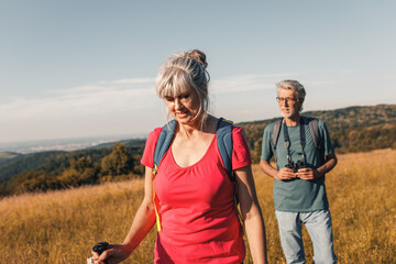 Wall Mural - Active senior couple hiking in nature with backpacks, enjoying their adventure in nature.