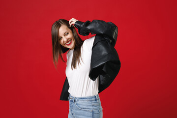 Wall Mural - Side view of smiling cheerful young brunette woman 20s wearing basic casual black leather jacket white t-shirt looking aside put hand on head isolated on bright red colour background studio portrait.