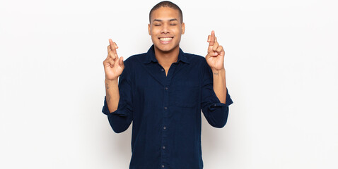 Sticker - young black man smiling and anxiously crossing both fingers, feeling worried and wishing or hoping for good luck