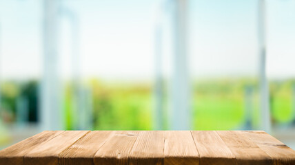 The top of the wooden table on the blur of the windowpane. Green color from a vegetable garden on the morning background. For product montage display.