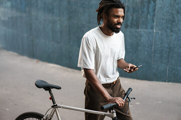 Wall Mural - African american guy using cellphone while walking with bicycle