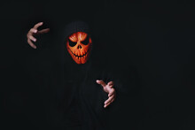 Horror Devil Costume With Spooky Pumpkin Skull In Black Dressed For Halloween Carnival. Devil Cosplay In Ghost Mask And Raise Hand With Blank Copy Space For Your Advertising Content.